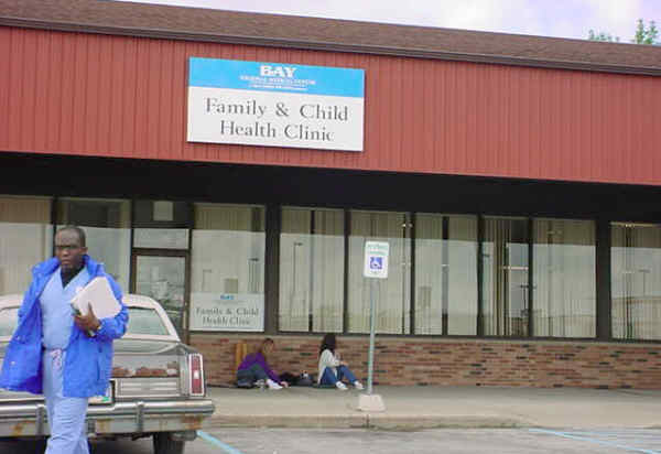 One of nearly two dozen volunteer health care providers walks past patients sitting on the sidewalk awaiting opening of thefree health clinic run by Bay Medical Center at the Medical Mall in Essexville.