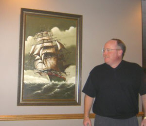 Spencer Dambro shows off his favorite art, an old painting of a square-rigger that once graced the Amerwood Inn on Genesee, run by his parents.