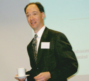 Carl Tannenbaum balances a coffee cup as he tosses out one-liners to explain his 